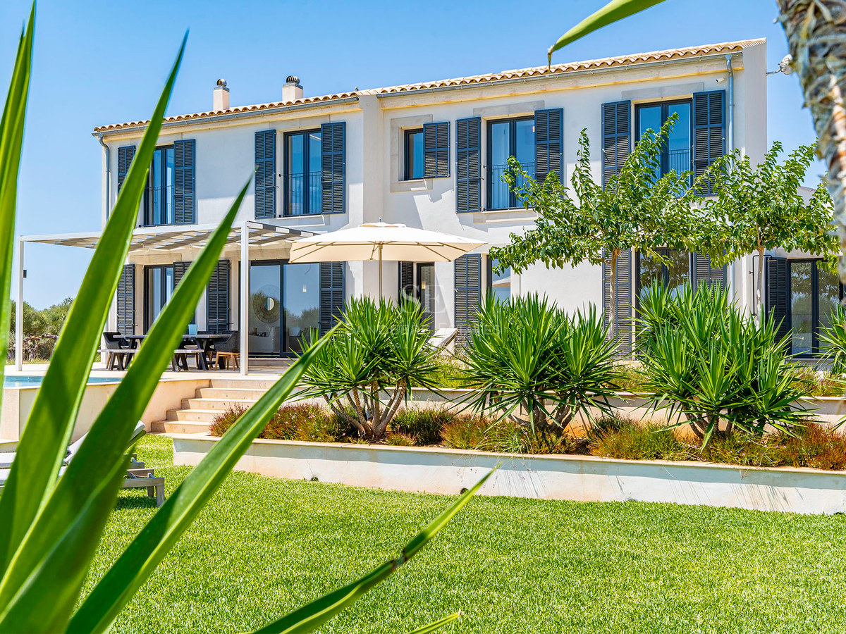 Villa blanche à deux étages avec volets gris, jardins en terrasses et pelouse soignée sous un ciel bleu.