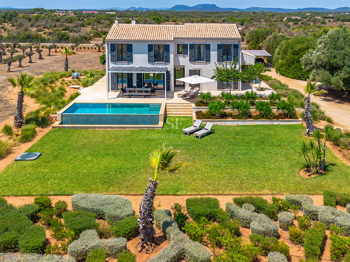Vue aérienne d'une villa gris clair avec toit en terre cuite, piscine à bordement et grande pelouse à Majorque.