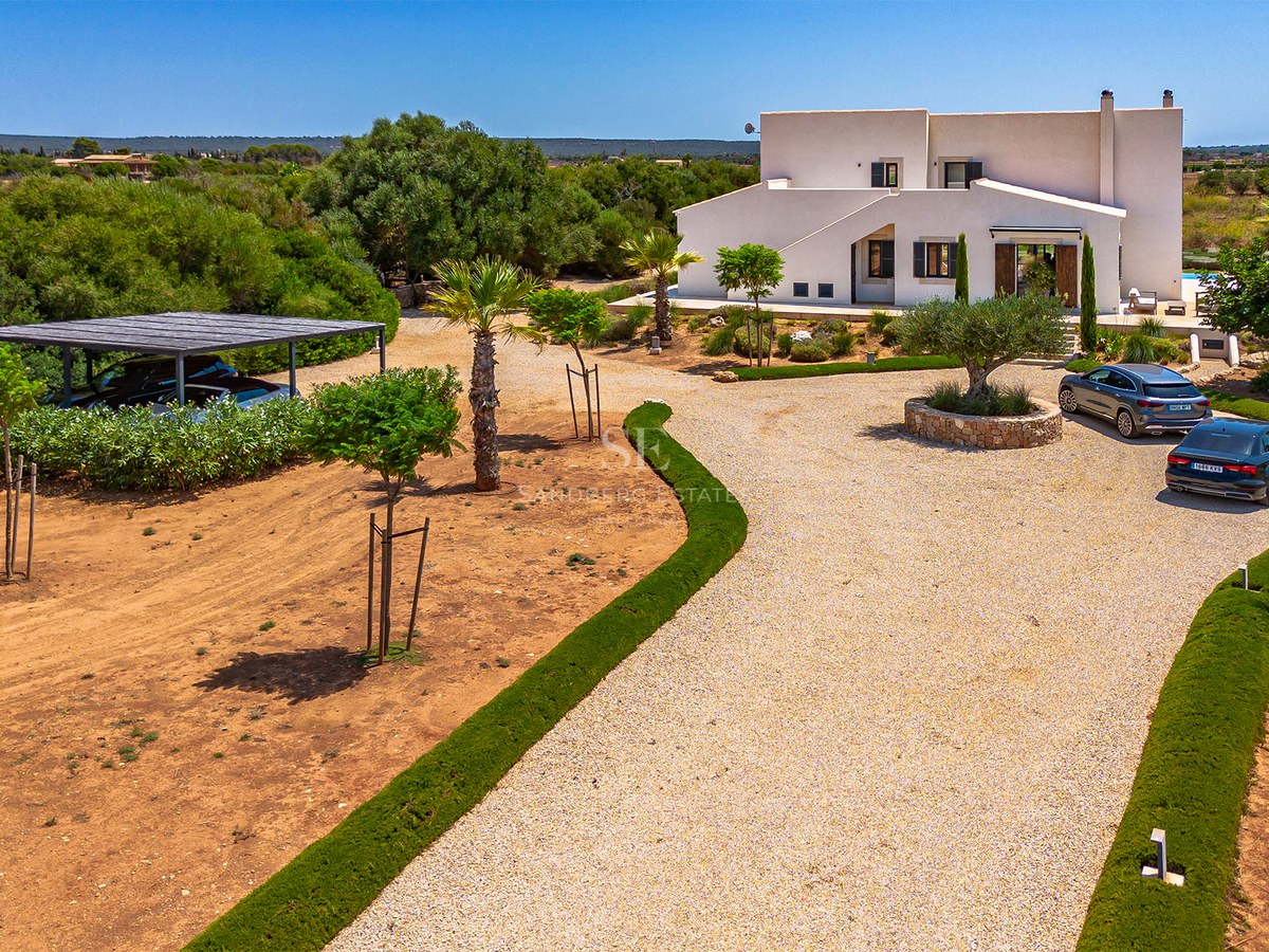 Vue aérienne d'une villa blanche contemporaine avec allée en gravier, jardin paysager et abri de voiture.