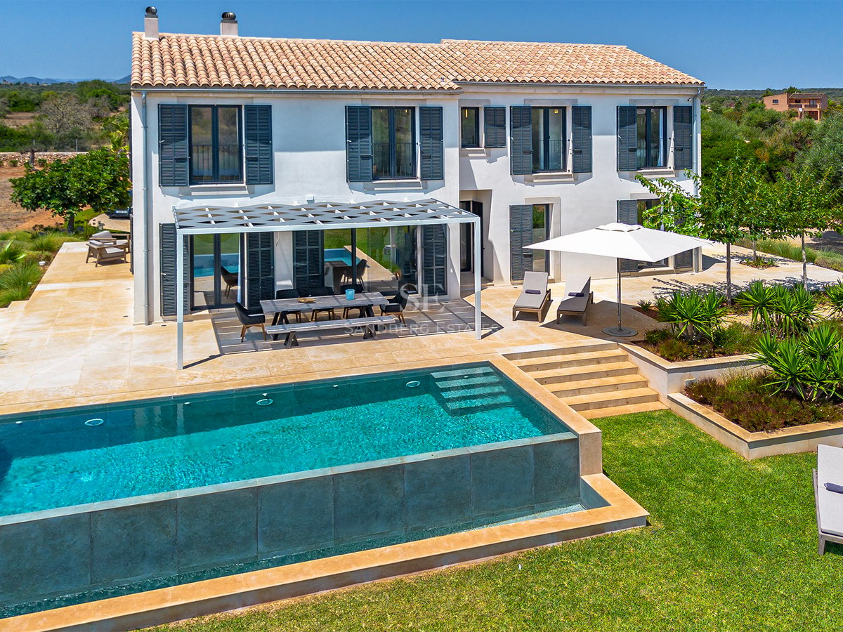 Vue extérieure d'une villa blanche avec piscine rectangulaire, terrasse en pierre et pergola moderne.