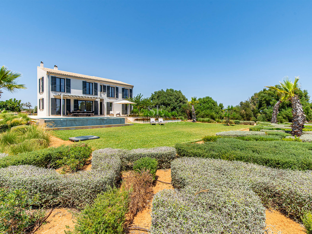 Villa de deux étages aux volets sombres, piscine et jardins soignés sous un ciel bleu dégagé.