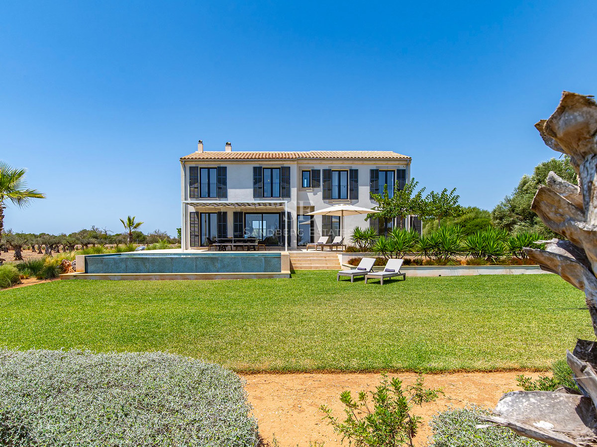 Villa beige à deux étages avec piscine à débordement, pelouse verte et volets sombres par temps clair.