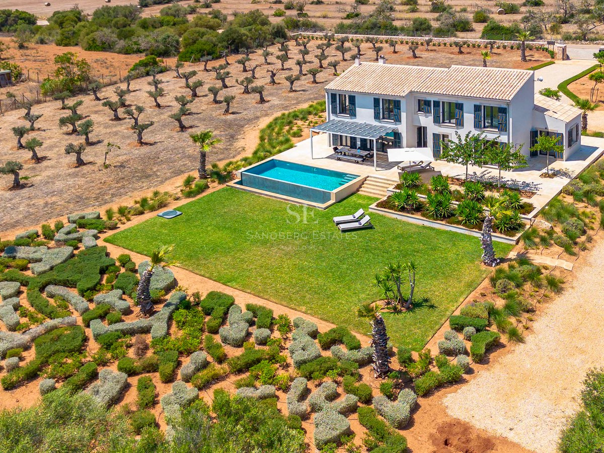 Vue aérienne d'une villa blanche à deux étages avec piscine à débordement, pelouse soignée et oliveraies environnantes.