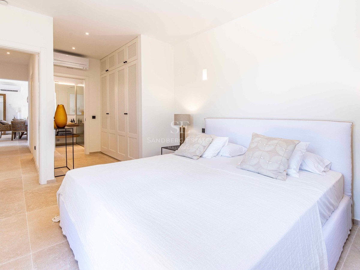 Chambre principale lumineuse avec linge de lit blanc, armoires encastrées et vue sur la salle de bains attenante.
