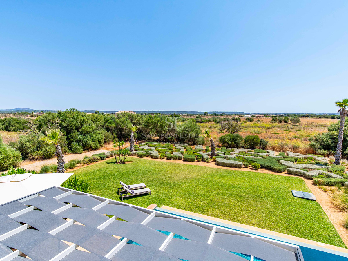 Vue depuis une terrasse avec pergola sur un vaste jardin paysager, des palmiers et la campagne environnante.