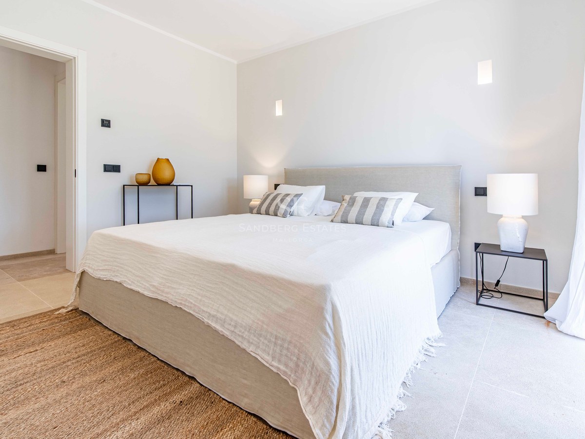 Chambre minimaliste avec sol en pierre, tapis en jute, grand lit et lampes de chevet modernes.