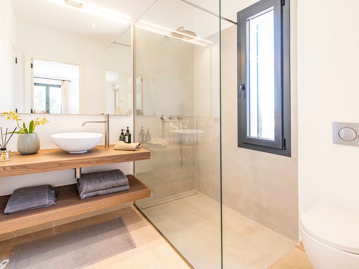 Salle de bains moderne avec douche vitrée, vasque à poser sur plan en chêne et grand miroir lumineux.