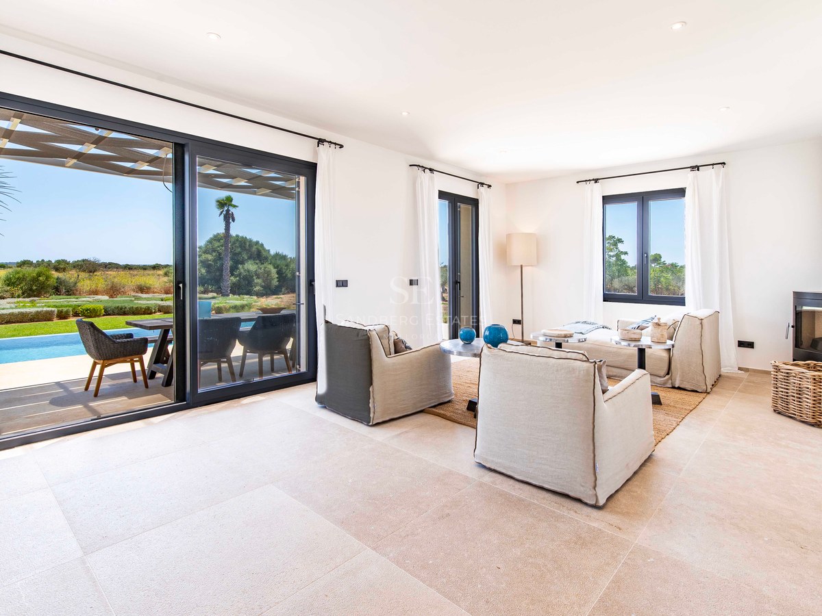 Salon lumineux avec baies vitrées s'ouvrant sur une terrasse avec piscine et jardin sous un ciel bleu.
