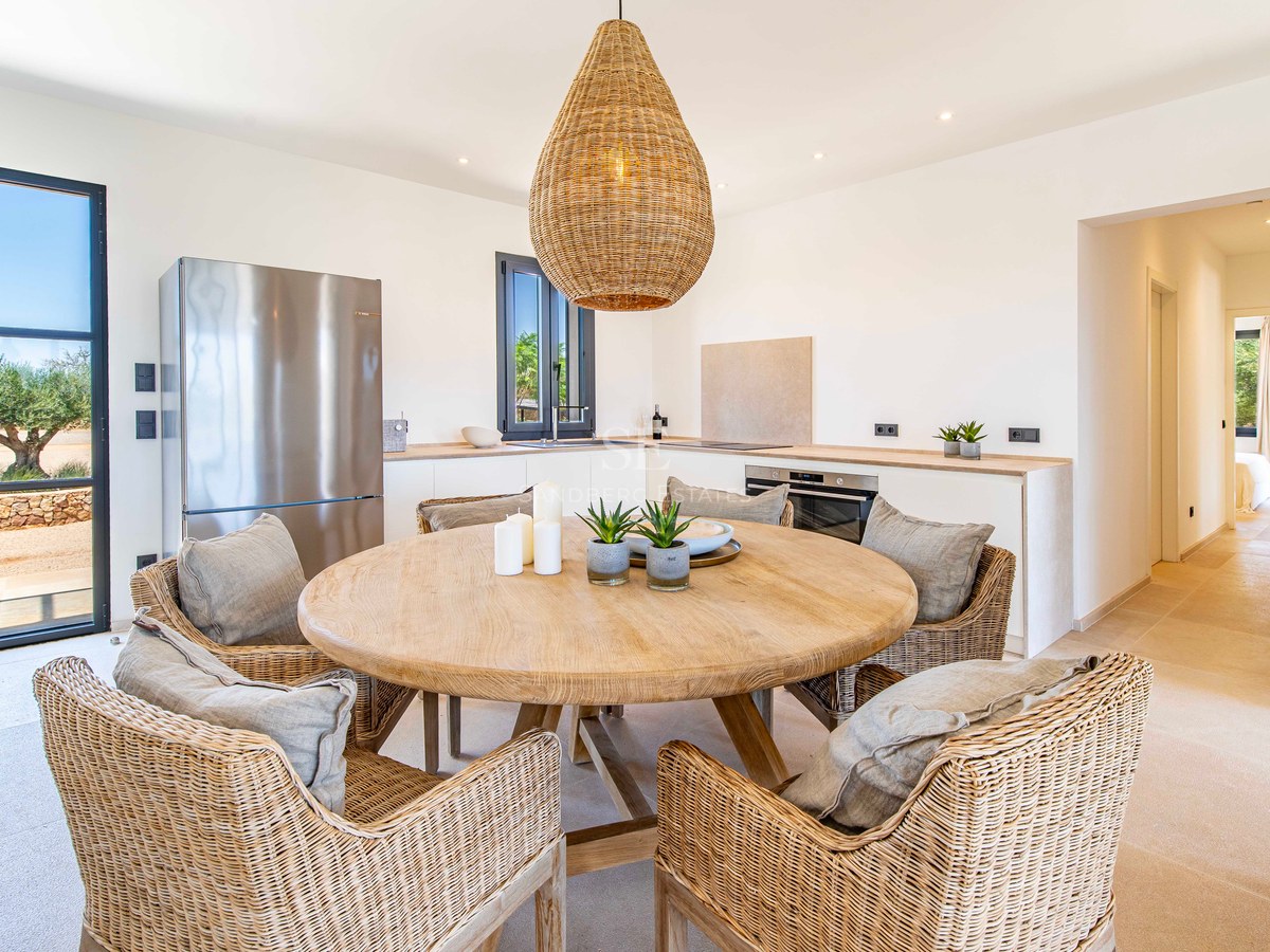 Table à manger ronde en bois avec six chaises en osier et suspension tressée dans une cuisine lumineuse.