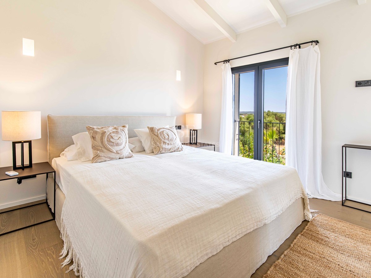Chambre lumineuse avec draps blancs, parquet en bois, plafond à poutres et porte vitrée donnant sur la verdure.