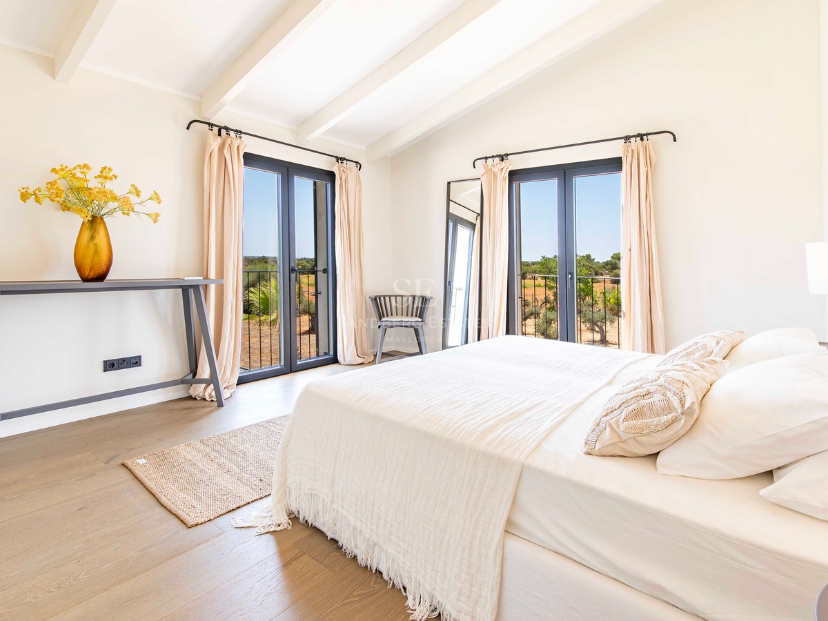 Chambre parentale lumineuse avec plafond voûté à poutres blanches, deux portes-fenêtres sombres et parquet en chêne.