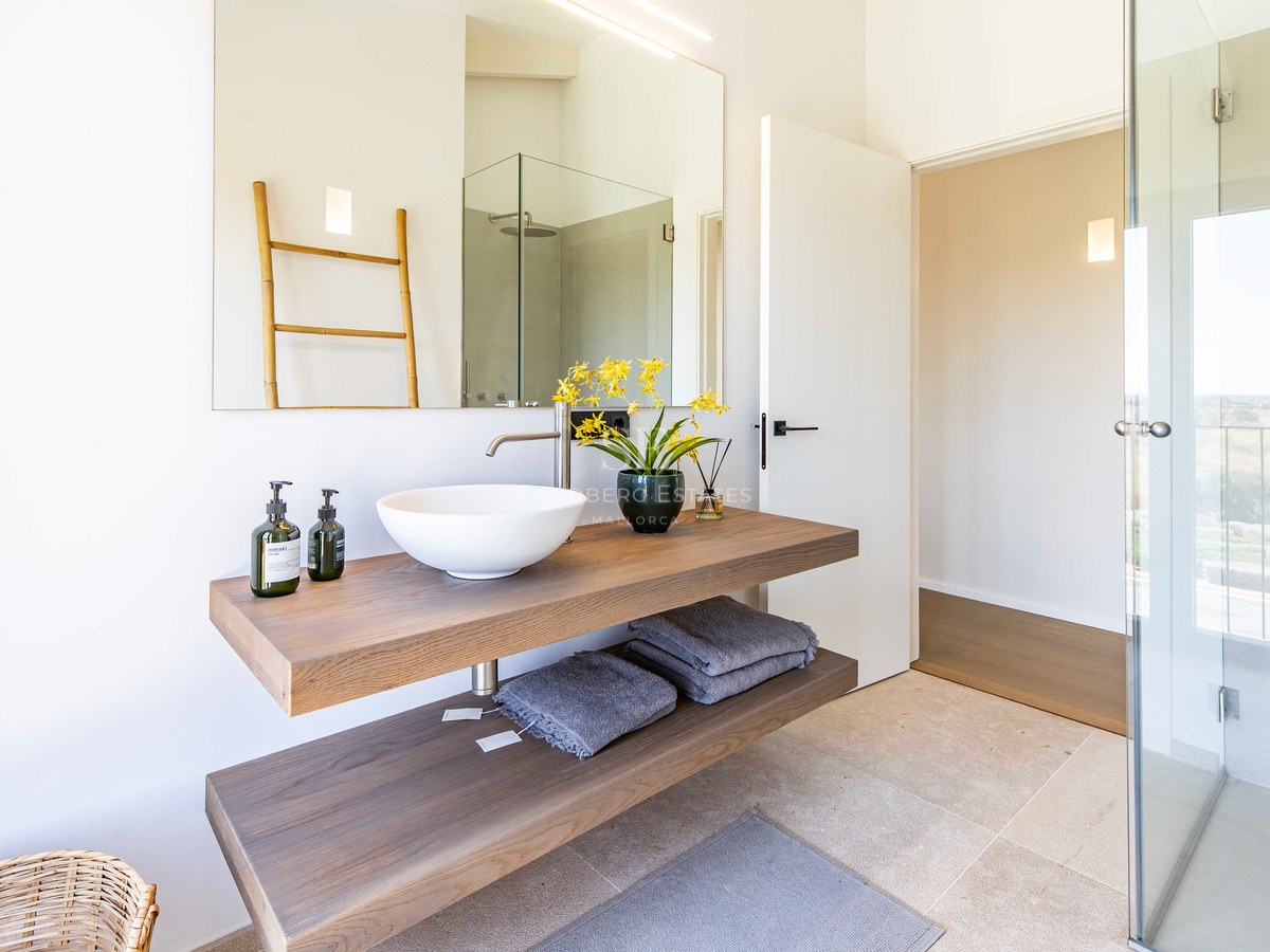 Salle de bain minimaliste avec meuble en chêne suspendu à deux niveaux, vasque blanche et grand miroir mural.
