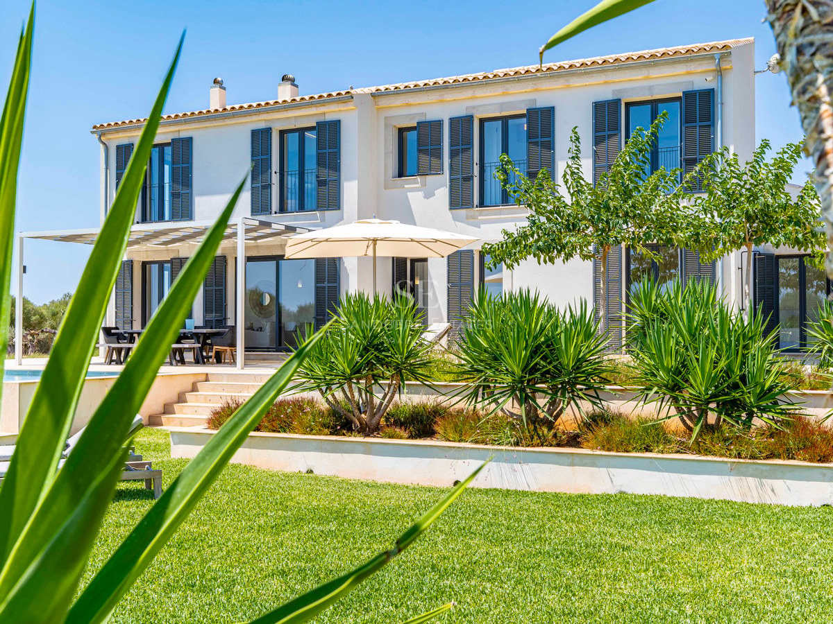 Villa blanche à deux étages avec volets bleus et jardins en terrasses sous un ciel bleu azur.