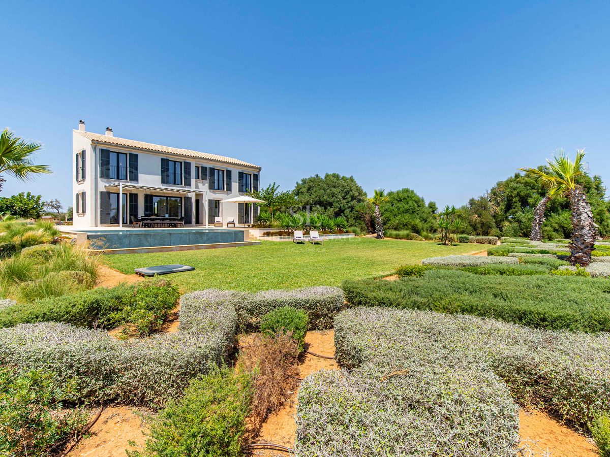 Vue extérieure d'une villa beige de deux étages avec piscine et jardins méditerranéens méticuleusement aménagés.