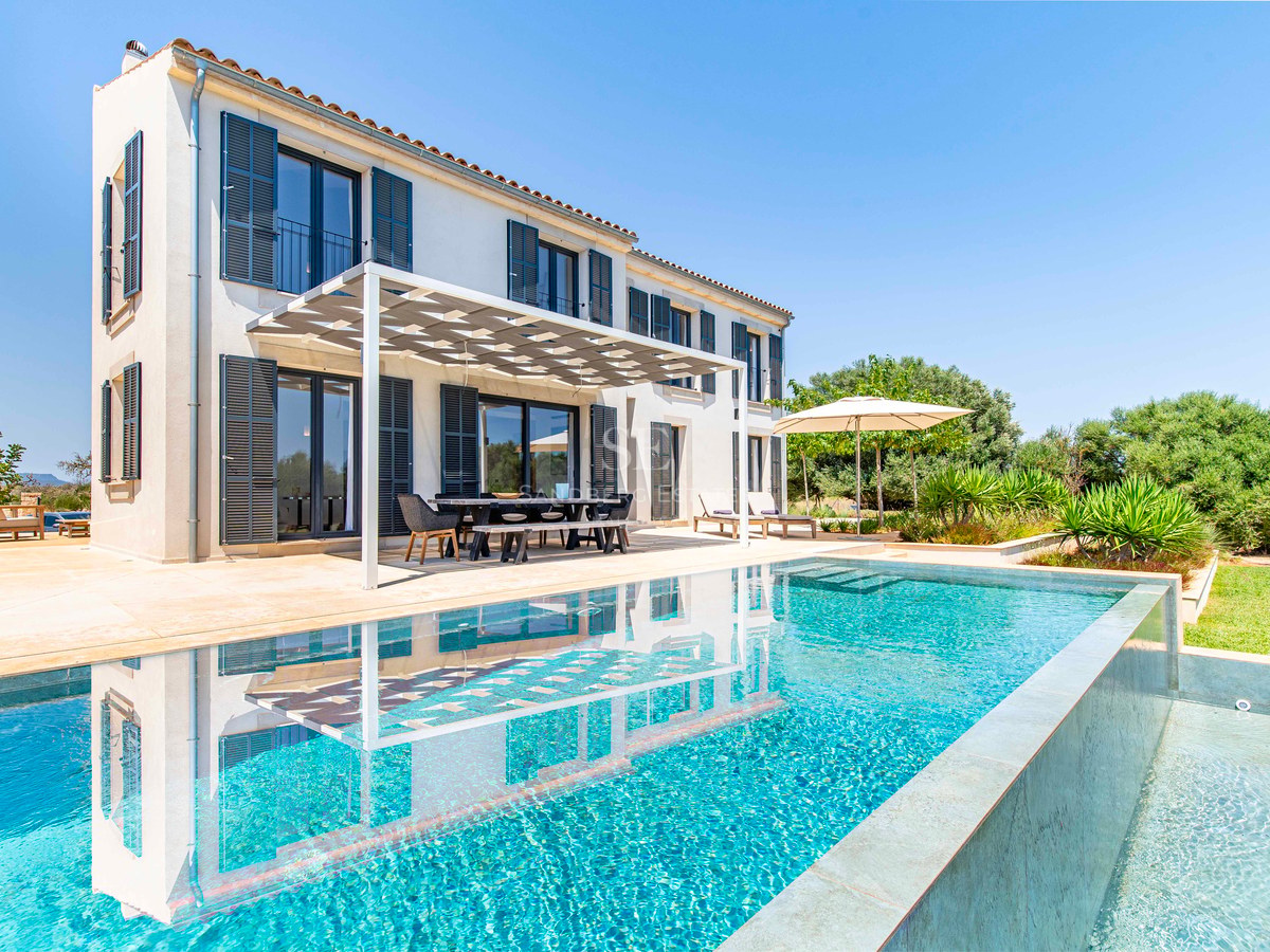 Extérieur d'une villa de luxe avec piscine turquoise et terrasse ombragée sous un ciel bleu azur.