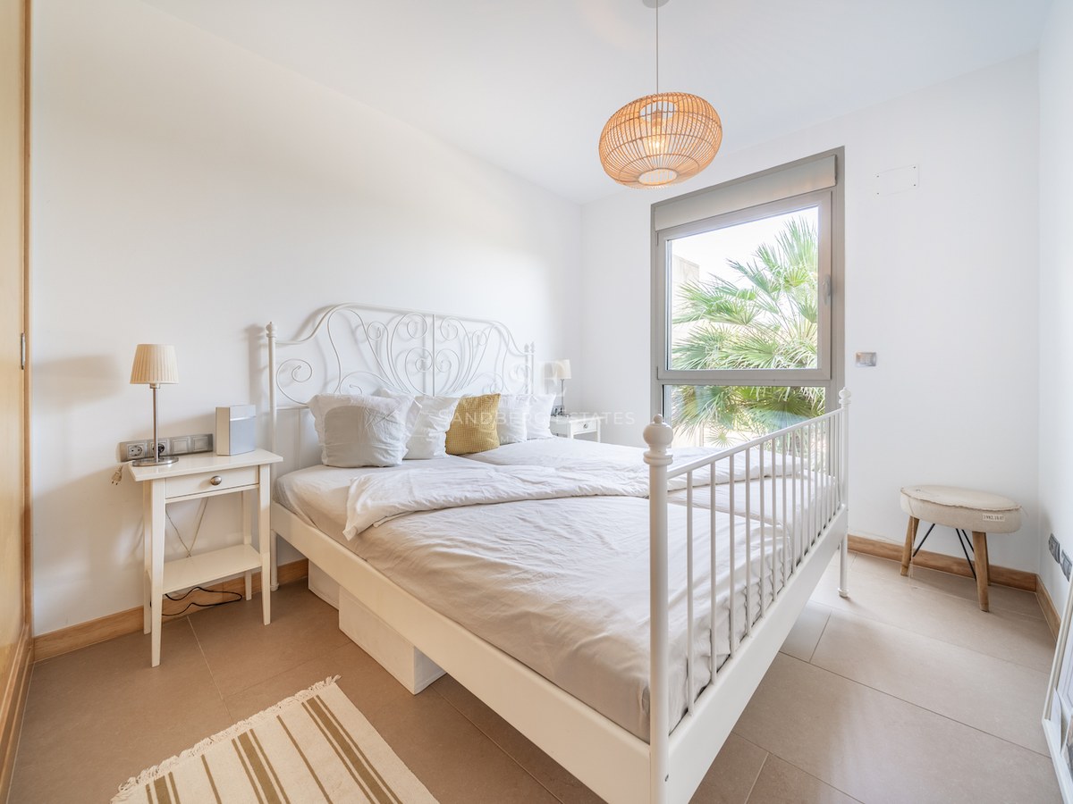 Bedroom featuring a white iron bed, built-in wooden wardrobe, and a window with a palm tree view.