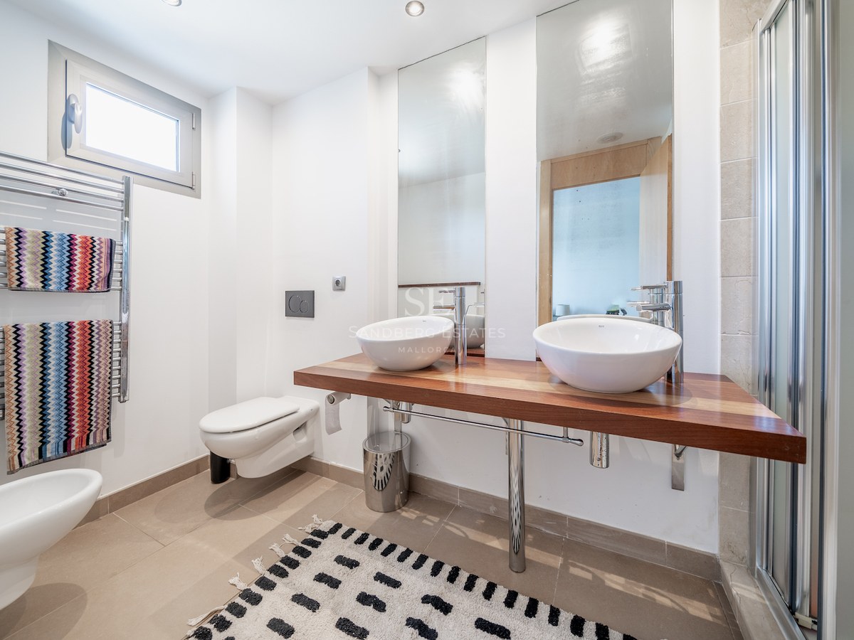 Bright bathroom with a wooden floating vanity, two white vessel sinks, heated towel rail, and large mirrors.