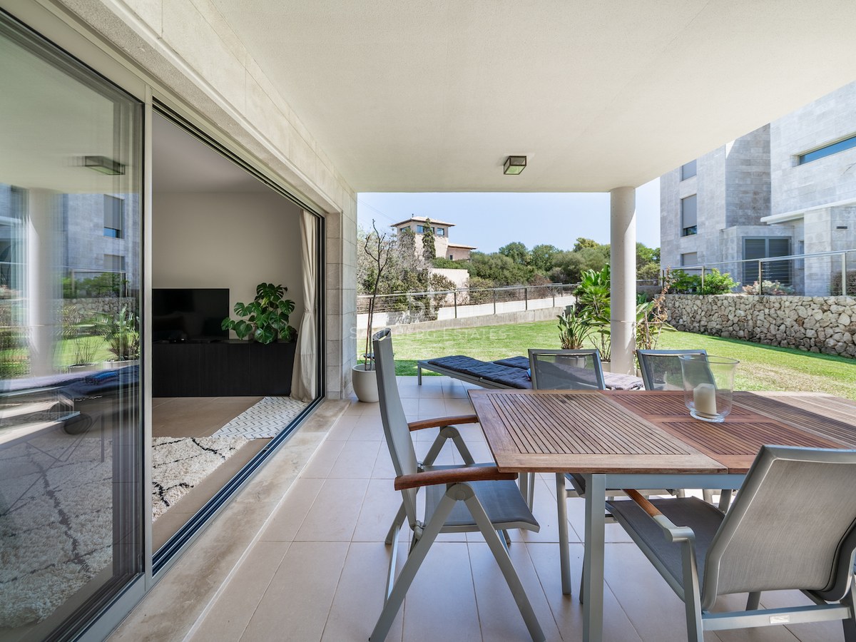 Covered terrace with wooden dining table and chairs leading to a private lawn and natural stone walls.