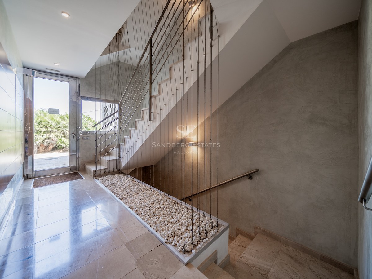 Bright entrance featuring polished stone floors, a staircase with cable railings, and a glass door to a garden.