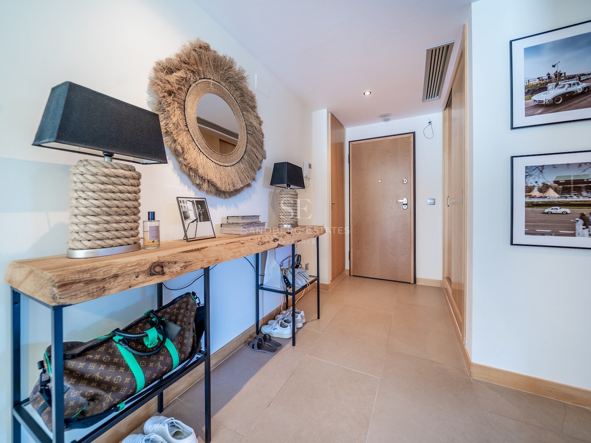 Modern entrance hallway featuring a live-edge wooden console table, round jute mirror, and warm beige tiling.