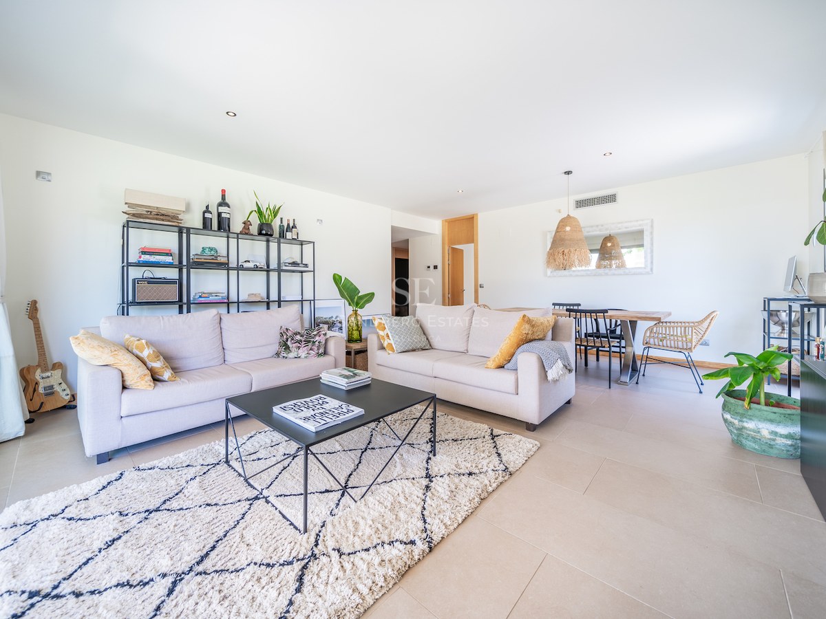 Spacious living room featuring neutral sofas, a geometric wool rug, black metal shelving, and an integrated dining area.