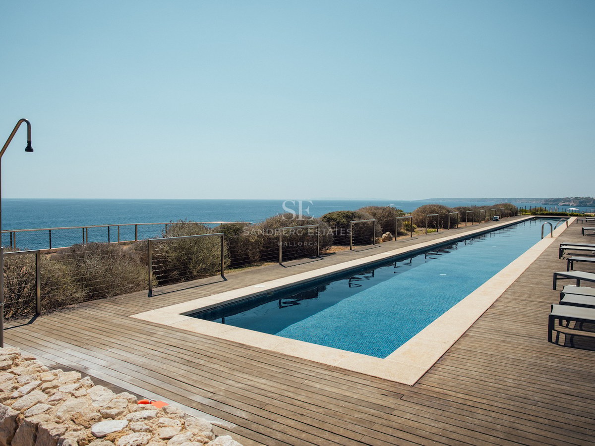 Long rectangular lap pool on a wooden deck overlooking the blue ocean with sun loungers and an outdoor shower.