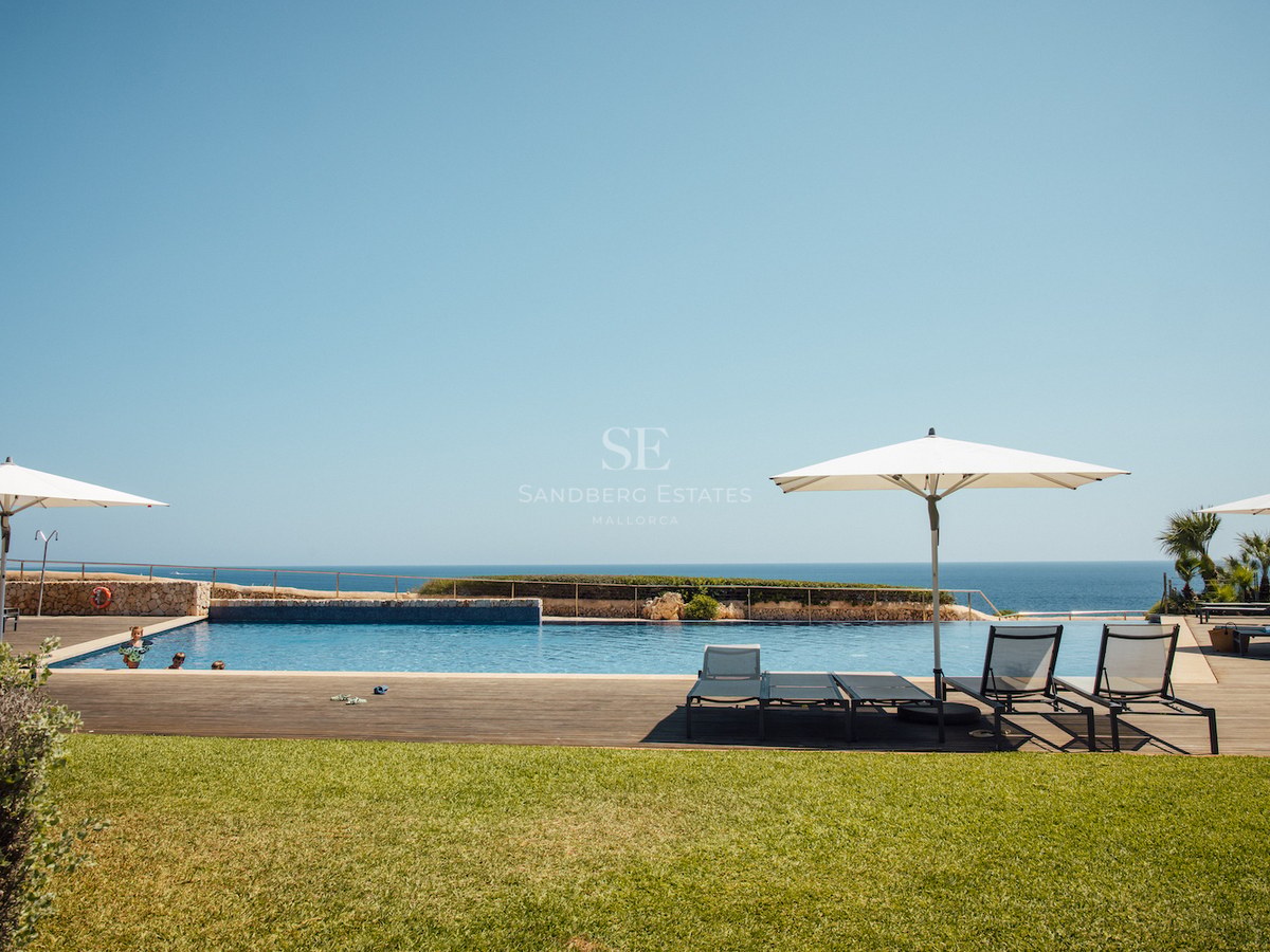 Large outdoor pool with wooden deck and sun loungers overlooking the sea under a clear blue sky.