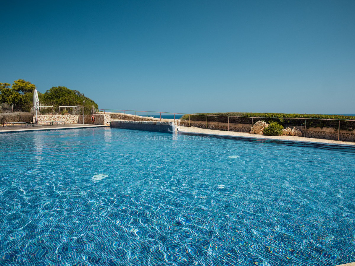 A large blue tiled swimming pool surrounded by natural stone walls and a metal railing under a clear blue sky.