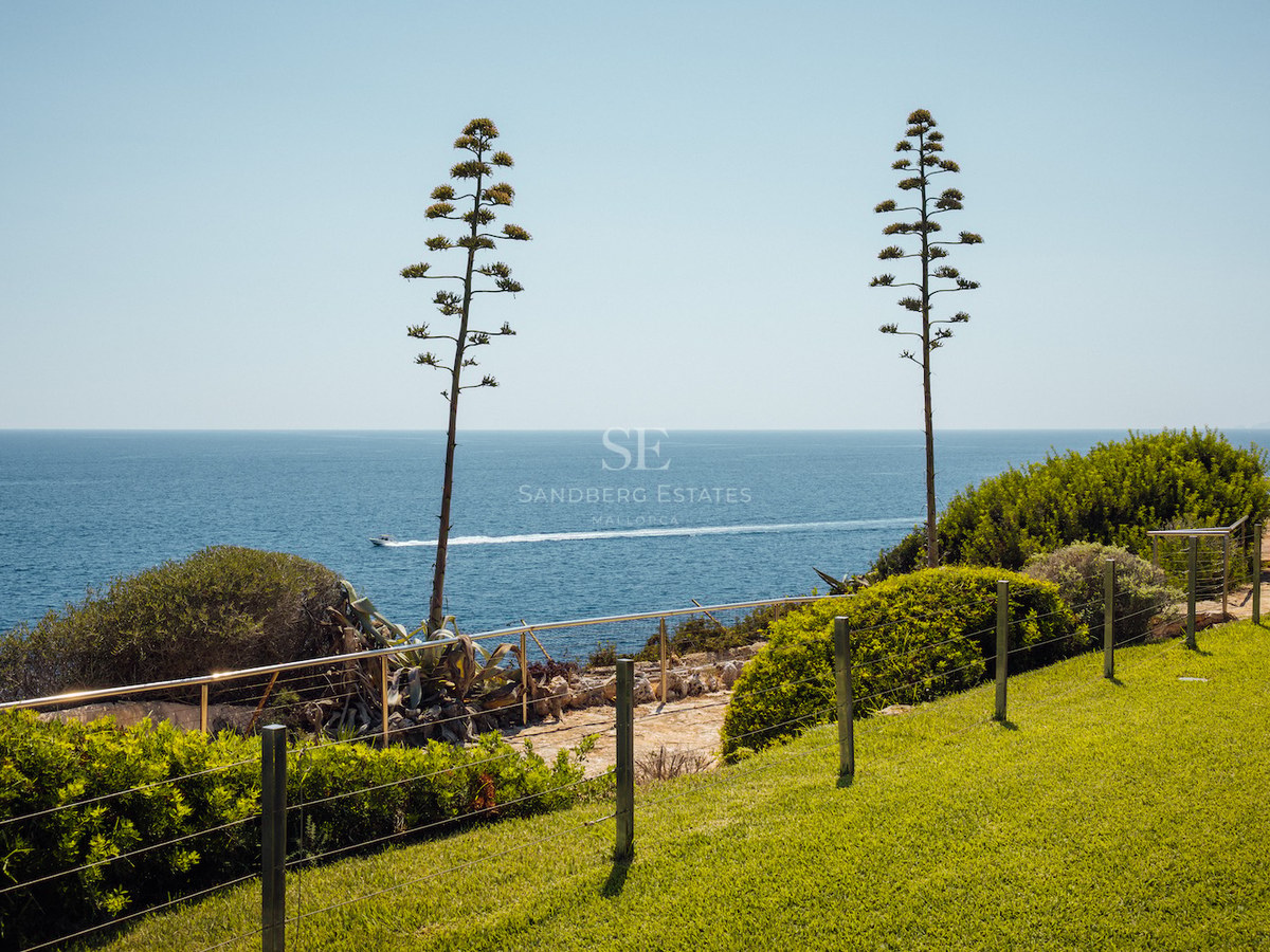 Coastal garden with a green lawn, two tall agave spikes, and an expansive view of the blue sea with a boat on the horizon.