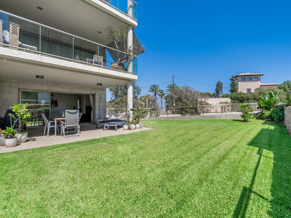 Covered ground floor terrace with outdoor dining area opening onto a manicured green lawn under a clear blue sky.