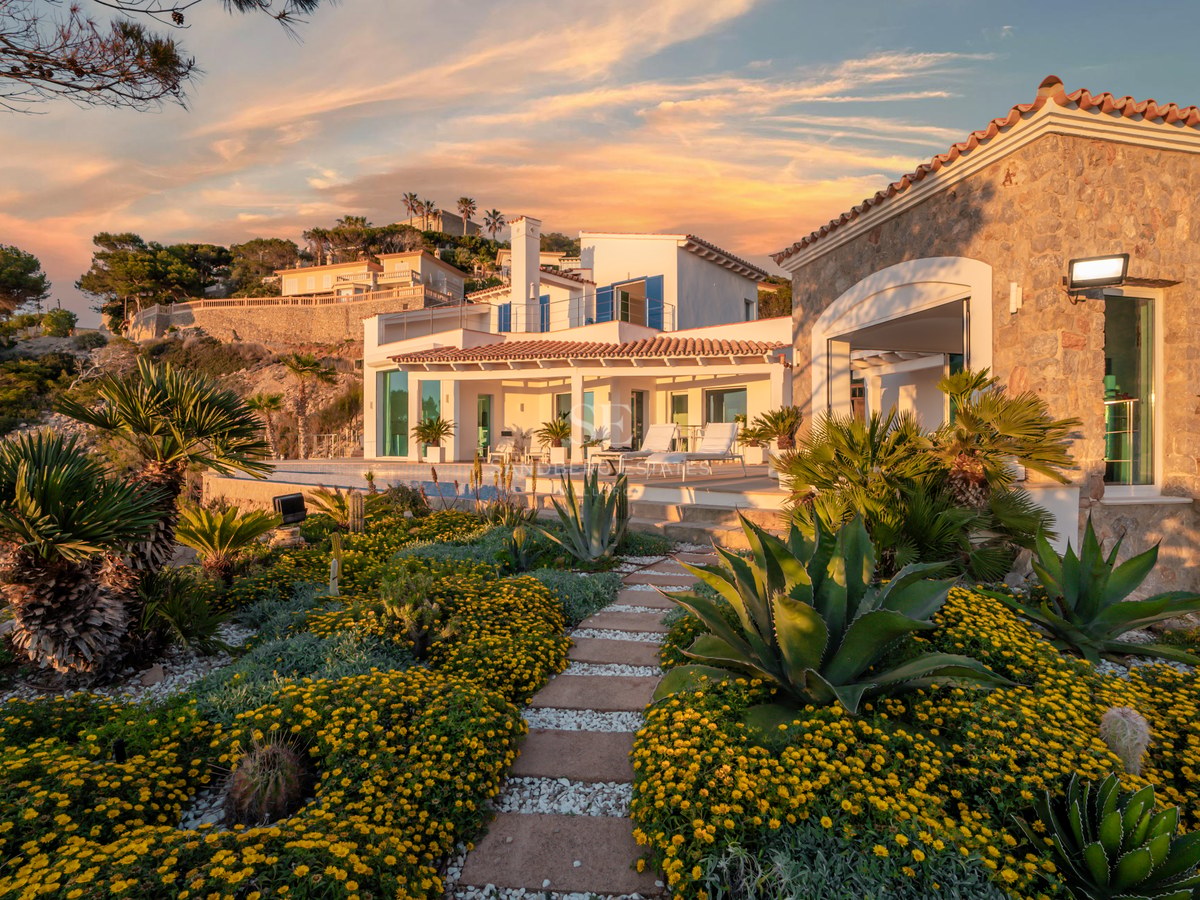 A modern Mediterranean villa at sunset featuring a landscaped garden with agave, yellow flowers, and an infinity pool.