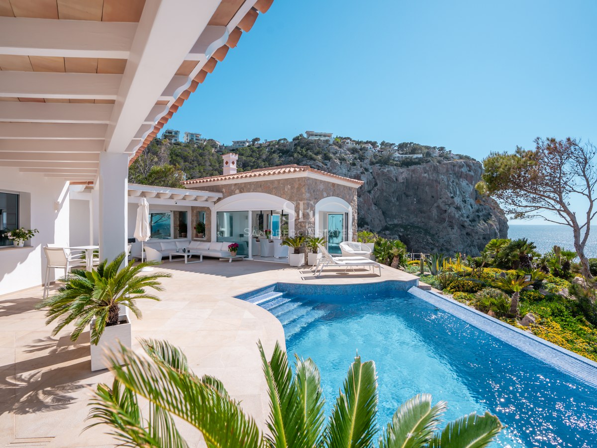 Curved infinity pool on a natural stone terrace overlooking coastal cliffs and the Mediterranean Sea.