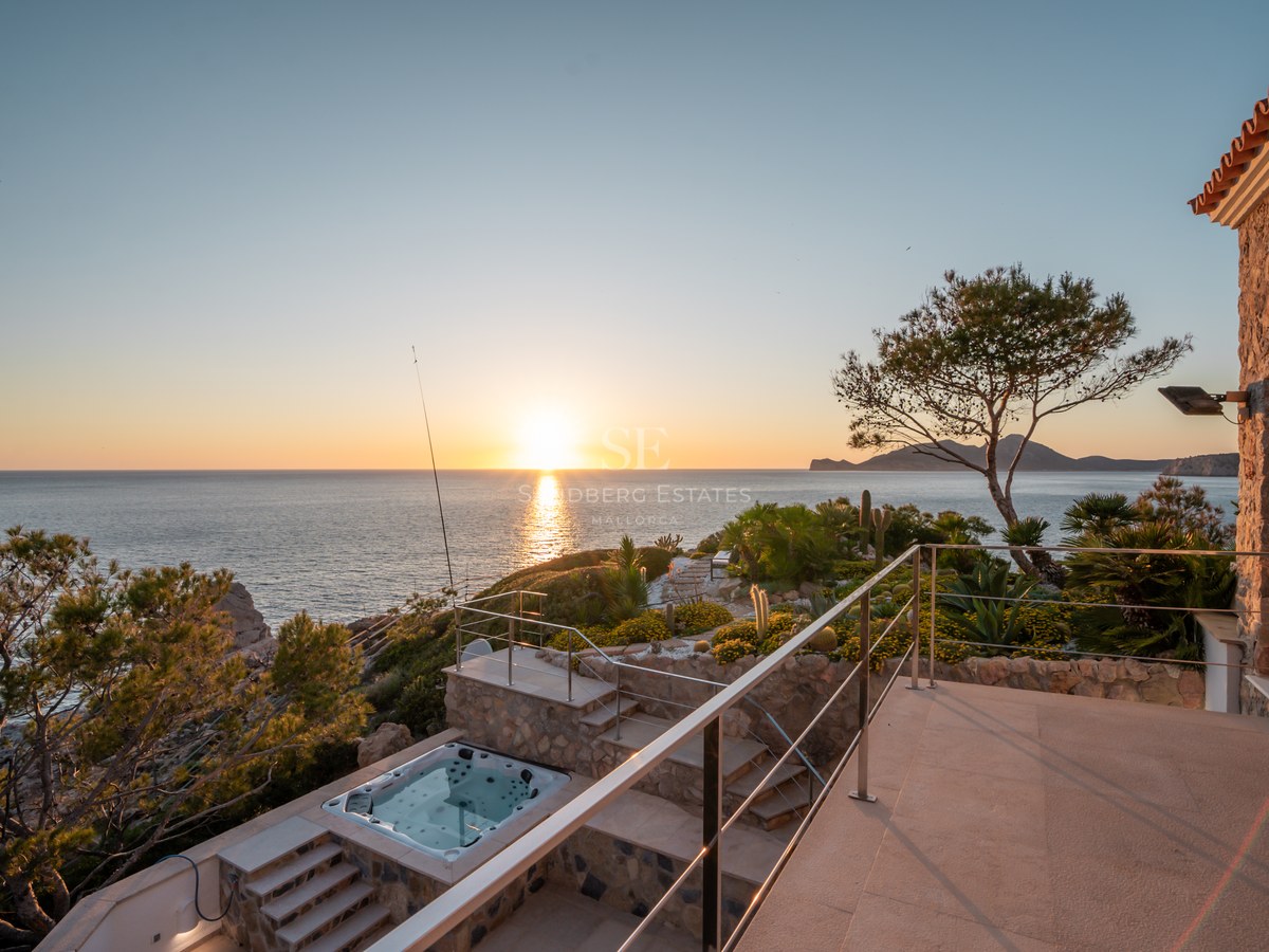 A multi-level stone terrace with a built-in jacuzzi overlooks the Mediterranean sea during a golden sunset.