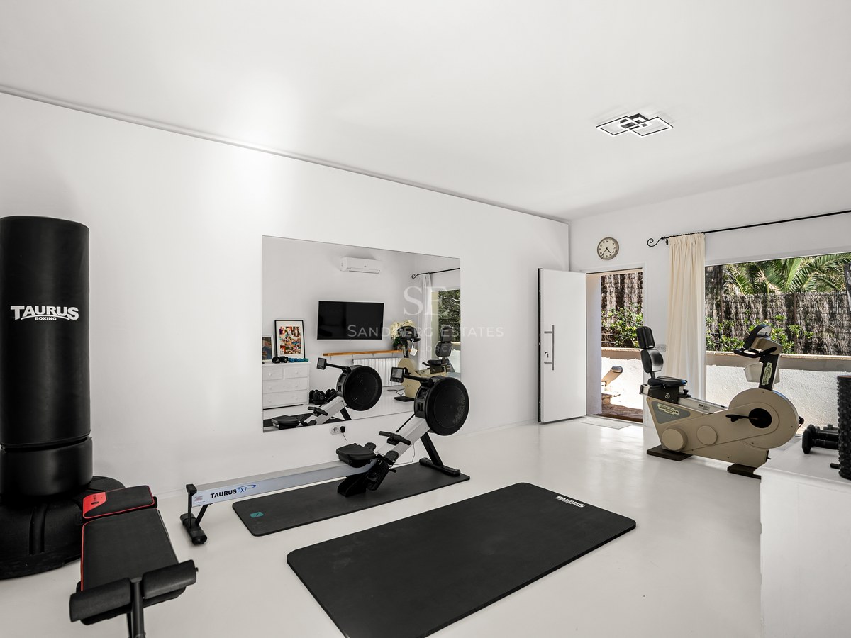 Modern white home gym with rowing machine, boxing bag, and exercise bike, featuring a large mirror and terrace access.