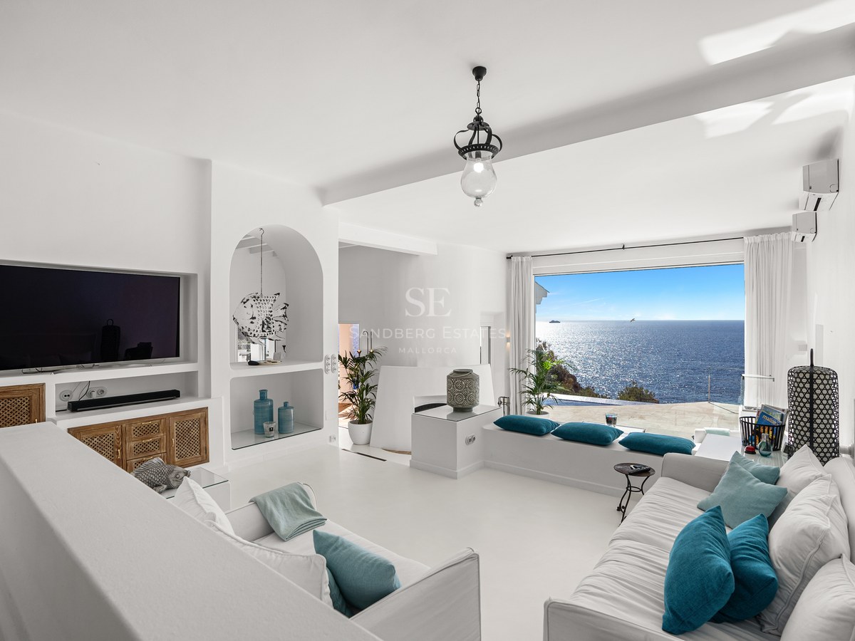 Bright white living room with turquoise cushions and a large window overlooking the sparkling Mediterranean Sea.