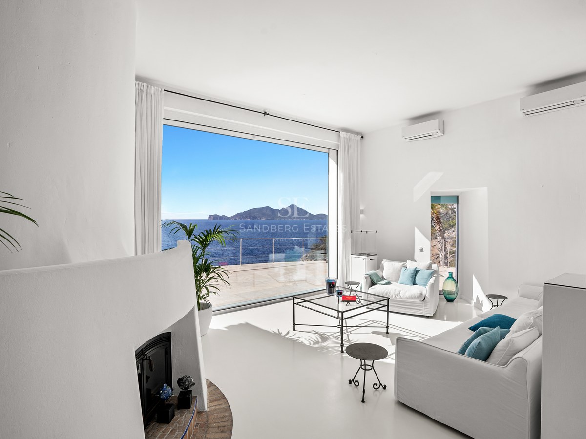 Bright white living room with a large picture window overlooking the Mediterranean sea and a distant island.