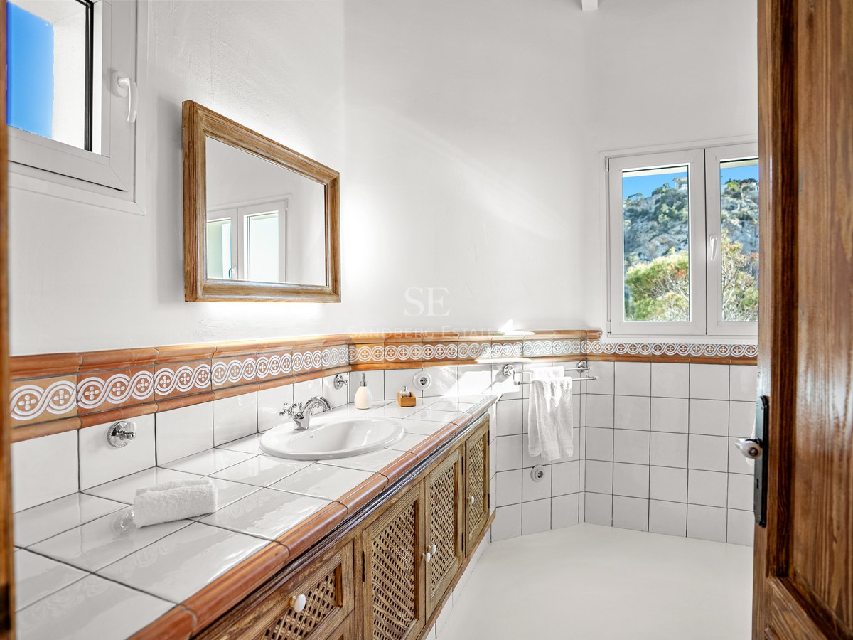 Bright bathroom featuring white tiles, terracotta accents, a wooden lattice vanity, and mountain views through windows.