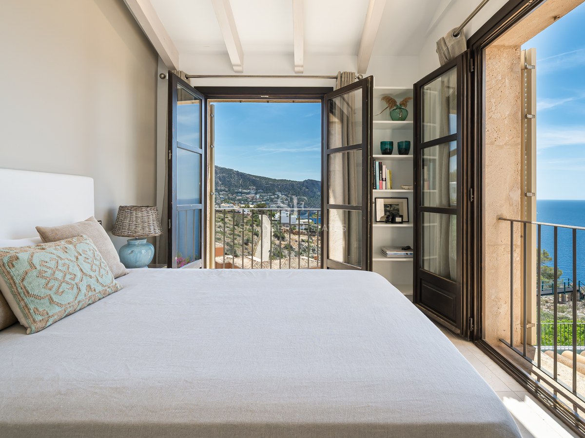 Chambre de luxe avec poutres blanches et portes-fenêtres ouvertes sur le littoral méditerranéen.