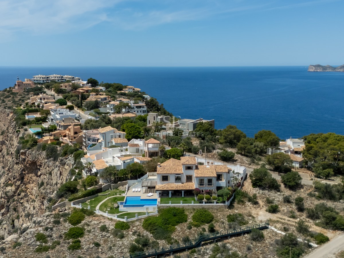 Vue aérienne d'une villa de luxe blanche avec piscine perchée sur une falaise rocheuse surplombant la Méditerranée.