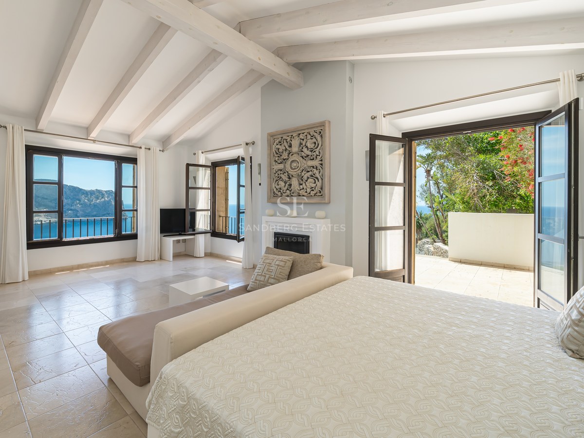 Chambre de maître lumineuse avec poutres blanches, sol en pierre et terrasse privée donnant sur la mer.