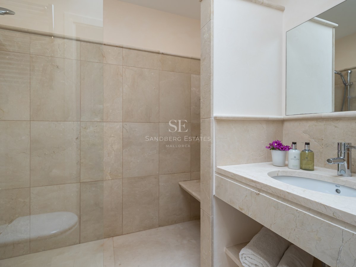 Salle de bains moderne avec carrelage en pierre beige, paroi de douche en verre et vasque intégrée en pierre.
