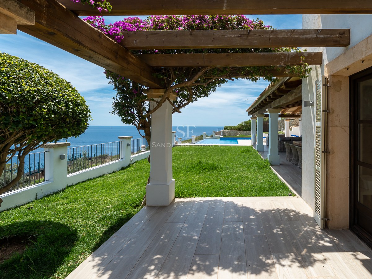 Terrasse ensoleillée avec pergola en bois, bougainvilliers et pelouse offrant une vue sur la mer Méditerranée.