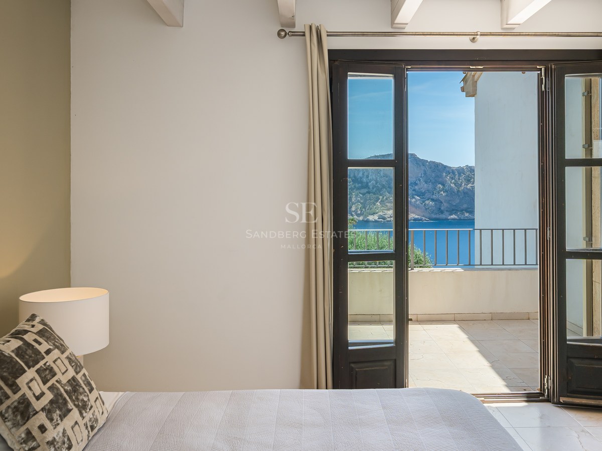 Chambre contemporaine avec poutres blanches et portes-fenêtres ouvrant sur une terrasse avec vue sur la Méditerranée.