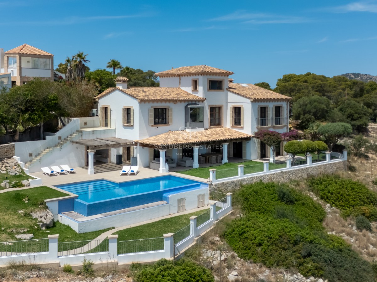 Vue extérieure d'une villa blanche méditerranéenne avec piscine bleue et toit en terre cuite par beau temps.