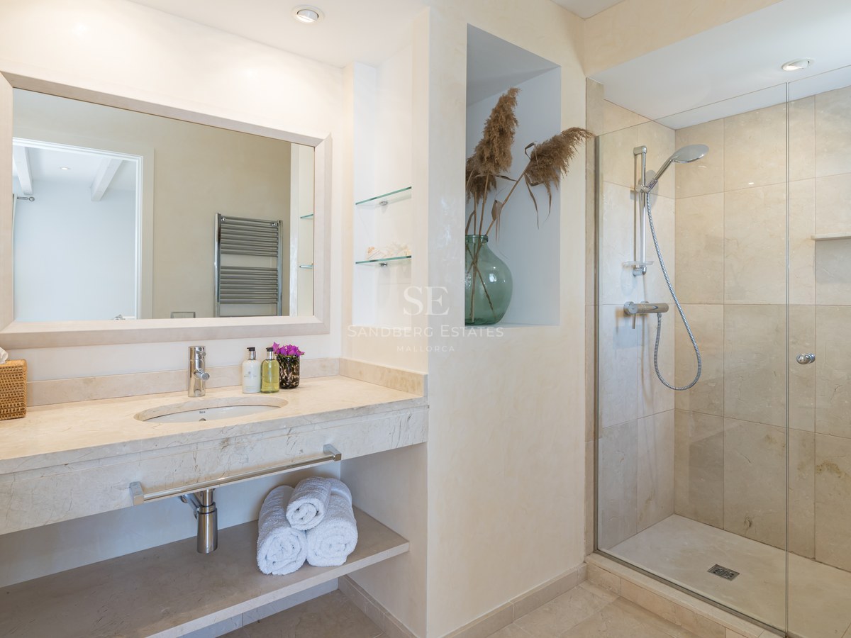 Salle de bain moderne avec douche à l'italienne, vasque en marbre beige et grand miroir à cadre blanc.