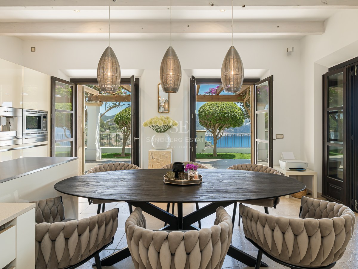 Cuisine moderne avec table ovale en bois sombre, suspensions design et portes vitrées ouvrant sur la mer.