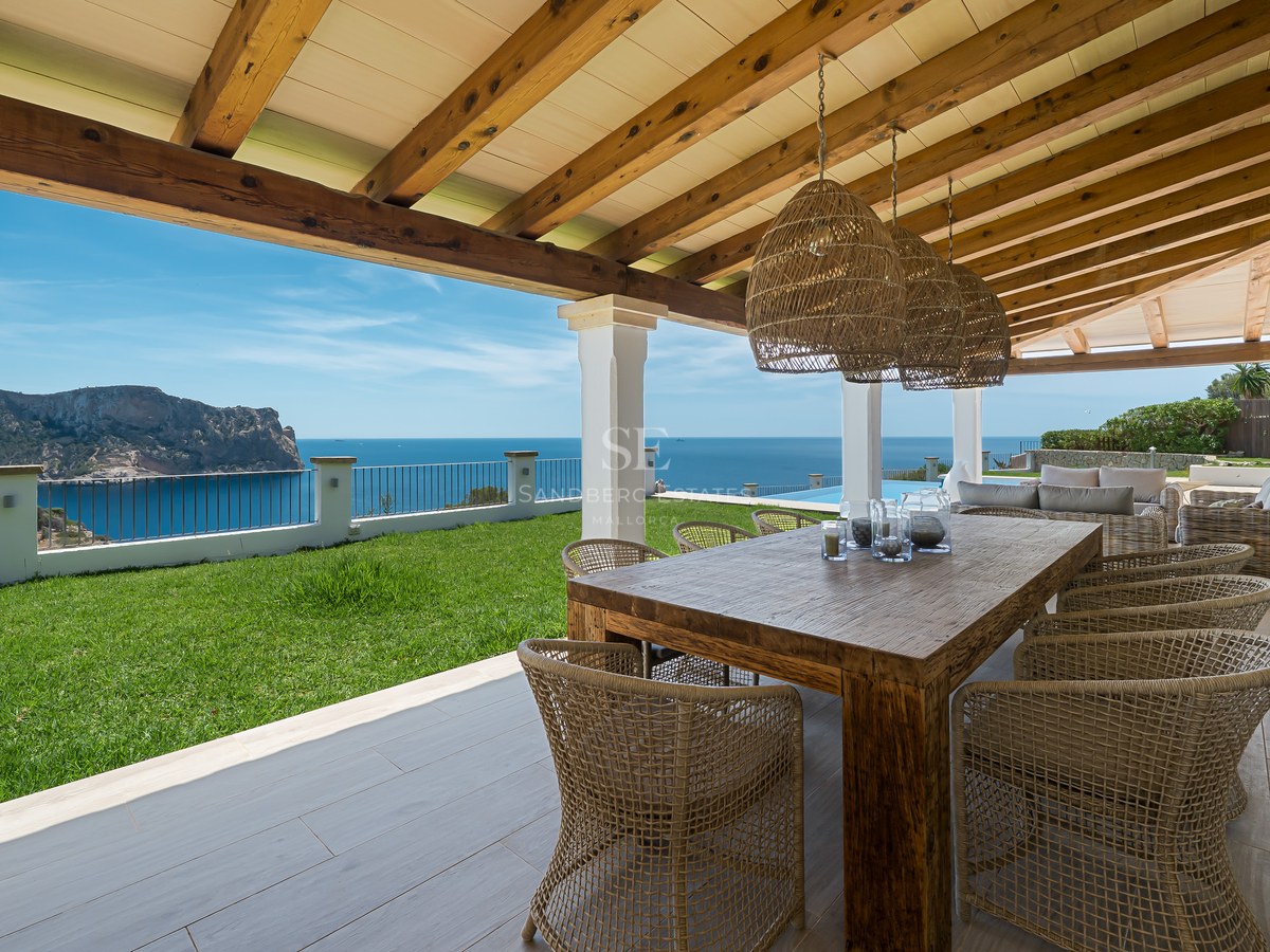 Grande table à manger en bois sous une terrasse couverte avec poutres apparentes, surplombant la mer Méditerranée.