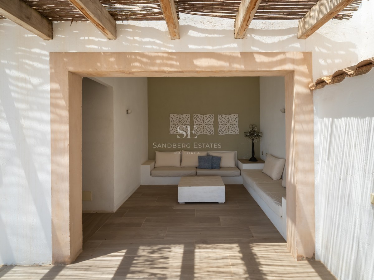 Salon de jardin ombragé avec canapés intégrés sous une pergola en bois et canisse, encadrement en pierre naturelle.