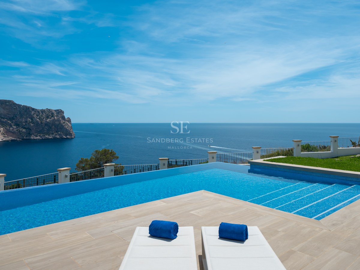 Piscine à débordement surplombant la mer Méditerranée avec une grande falaise rocheuse en arrière-plan sous un ciel bleu.