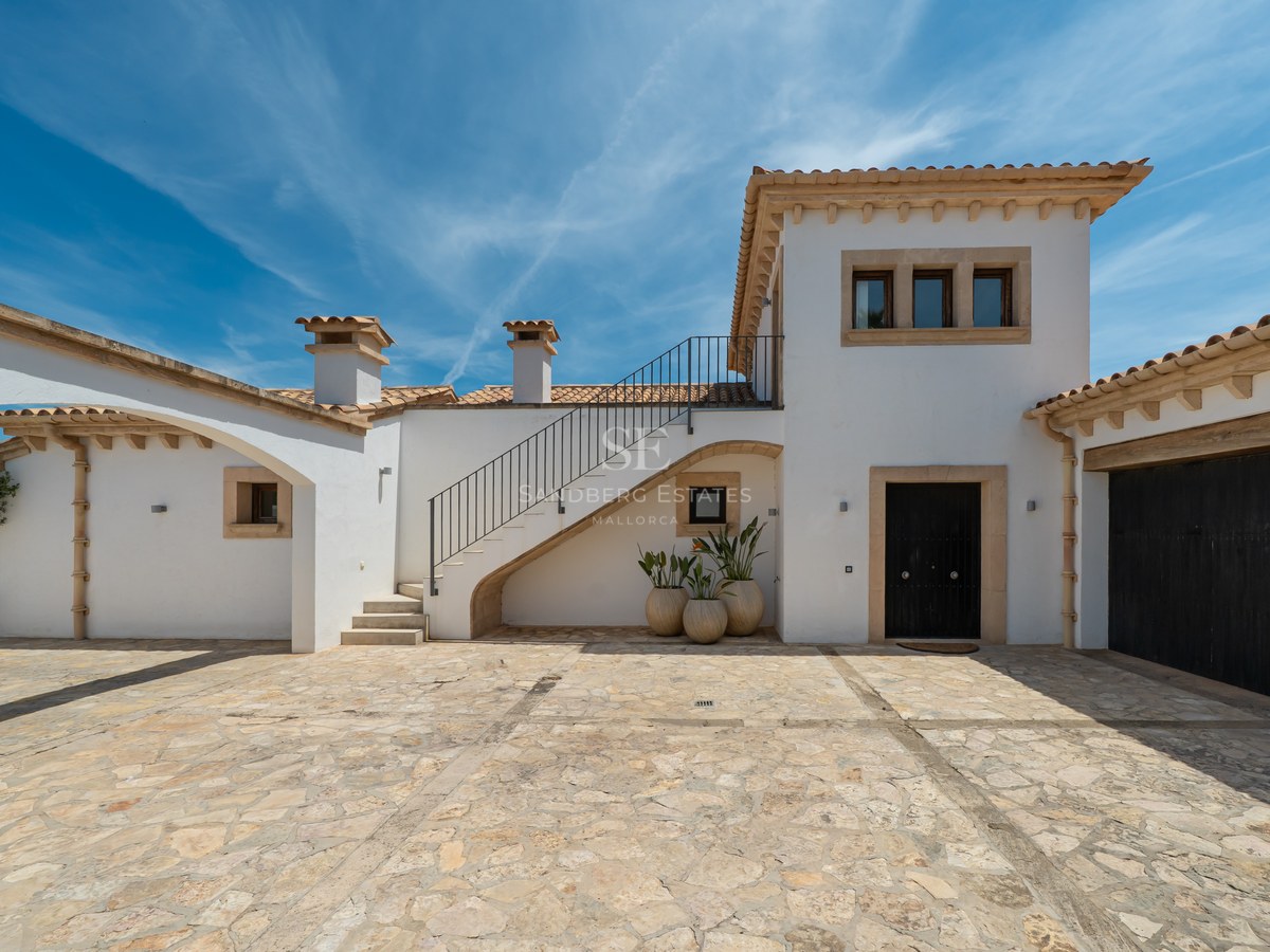 Façade de villa blanche avec cour en pierre naturelle, toit en terre cuite et escalier extérieur par temps clair.